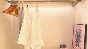 A neatly organized closet with hanging towels, a folded towel stack, and a framed picture on a shelf. - S Gen Residences Phu Quoc (Phu Quoc)