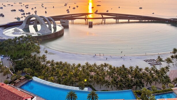 A resort with a large swimming pool, a circular water feature, and a beach area with palm trees. - S Gen Residences Phu Quoc (Phu Quoc)