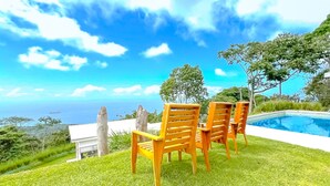 A poolside area with wooden chairs and a view of the ocean. - Casa Lapa (Bahía Ballena)