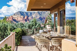 An outdoor patio with wicker furniture and a table set for dining, overlooking a mountainous landscape. - Sedona Luxury with 75' Lap Pool, Hot Tub & Breathtaking Vortex Views (Sedona)