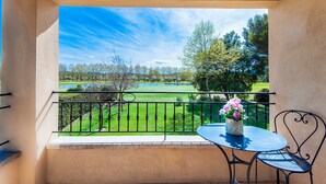 Un balcón con vista a un campo de golf, una mesa con un florero y una silla.