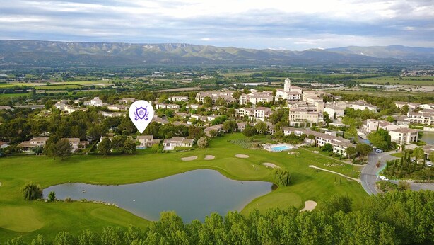 Un campo de golf con un estanque, rodeado de edificios residenciales y montañas al fondo.