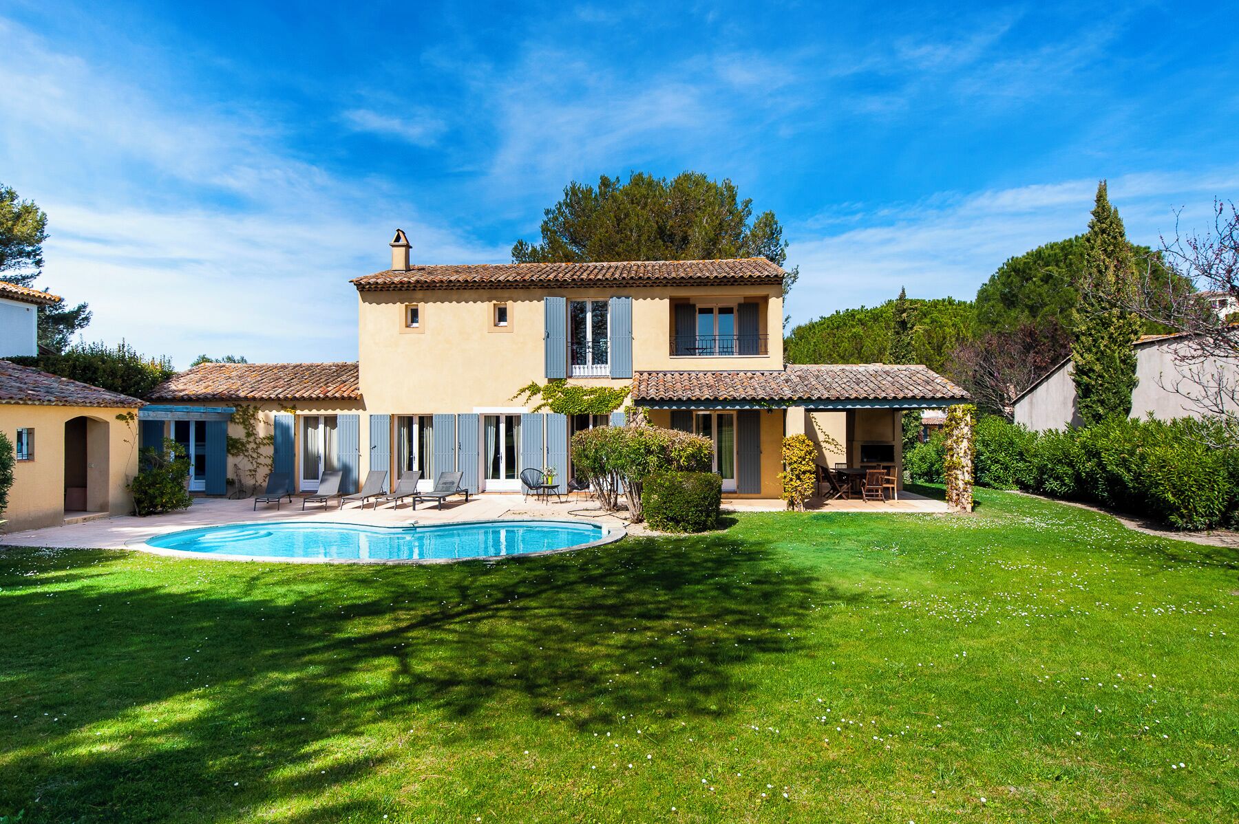 Une maison à deux étages avec une piscine, entourée d’une pelouse bien entretenue et d’arbres.
