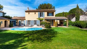 Una casa de dos pisos con piscina, rodeada de césped cuidado y árboles.