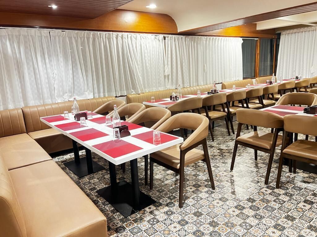 A conference room with rows of tables and chairs, a large window with curtains, and a patterned floor.