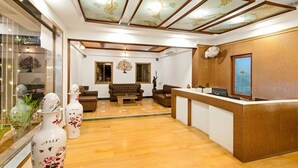 A reception area with a wooden reception desk, a sofa, and a coffee table. There are decorative vases on the left and a ceiling with leaf patterns. - Hotel Sapphire  (Mawal)