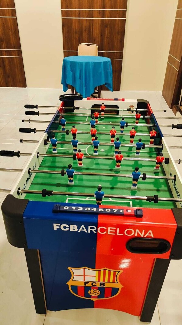 A foosball table with FC Barcelona branding, a blue tablecloth, and a small table with a blue cloth in the background. - Hotel Sapphire (Mawal)