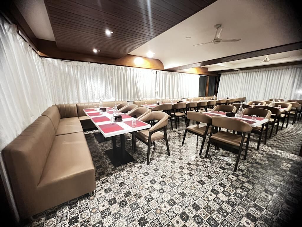 Un salón de conferencias con un sofá, mesas, sillas, alfombra estampada y cortinas.