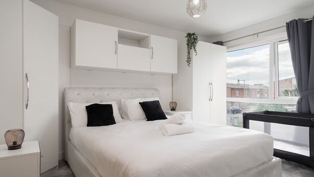 Un dormitorio con una cama grande, paredes blancas y vistas a la calle a través de una ventana.