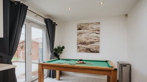 Una mesa de billar en una habitación con puerta corredera de vidrio, una planta en maceta y un cuadro en la pared.