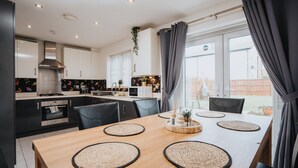 Una cocina moderna con armarios oscuros, una mesa de comedor de madera con individuales tejidos y vistas al patio trasero a través de ventanas amplias.