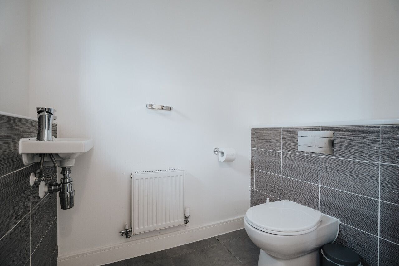 A modern bathroom with a toilet, a sink with a pipe, a radiator, and a wall-mounted toilet paper holder.