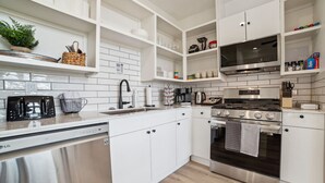 Una cocina moderna con armarios blancos, electrodomésticos de acero inoxidable y estantes abiertos.