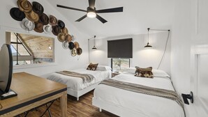 A modern bedroom with two beds, a desk, and a ceiling fan.