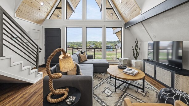 A spacious living area with a high ceiling, large windows, a staircase, and modern furnishings.