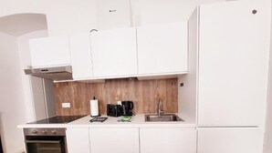 Une cuisine compacte avec des meubles blancs, un four encastré, une machine à café et un évier.