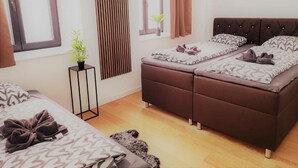 Une chambre avec deux lits, une petite table de chevet, une fenêtre avec des rideaux et une plante en pot.