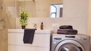 Une petite salle de bain équipée d’un lave-linge, d’un évier et d’une plante en pot.