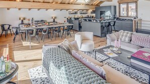 Amplia sala de estar con techo alto, vigas de madera, una mesa de comedor con sillas, un sofá y una zona de cocina con barra.
