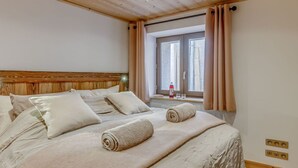 Una cama bien hecha con cabecera de madera, una ventana con cortinas y un dispensador de gel hidroalcohólico en la mesita de noche.
