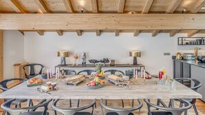 Comedor con una larga mesa de madera, sillas negras y una cocina al fondo.