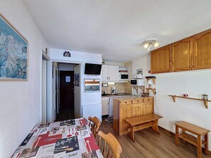 A compact kitchen with white cabinets, a microwave, and a coffee maker. There's a wooden bench and a small table.