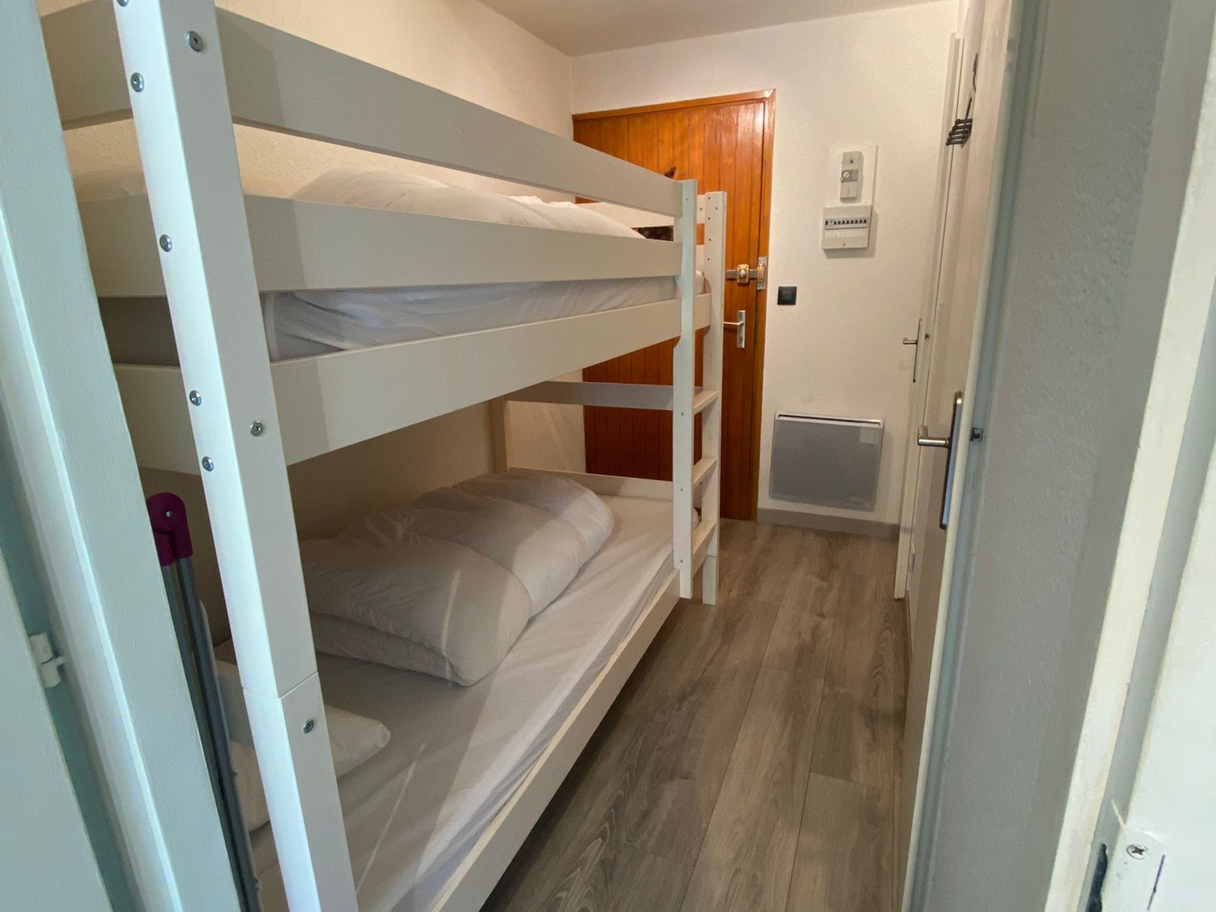 A bunk bed room with a wooden door and a thermostat on the wall.