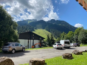 A parking area with a building, a white van, and a car.