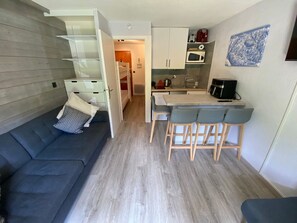 Um espaço de estar compacto com sofá, área de refeições com banquetas, cozinha com micro-ondas e piso de madeira.