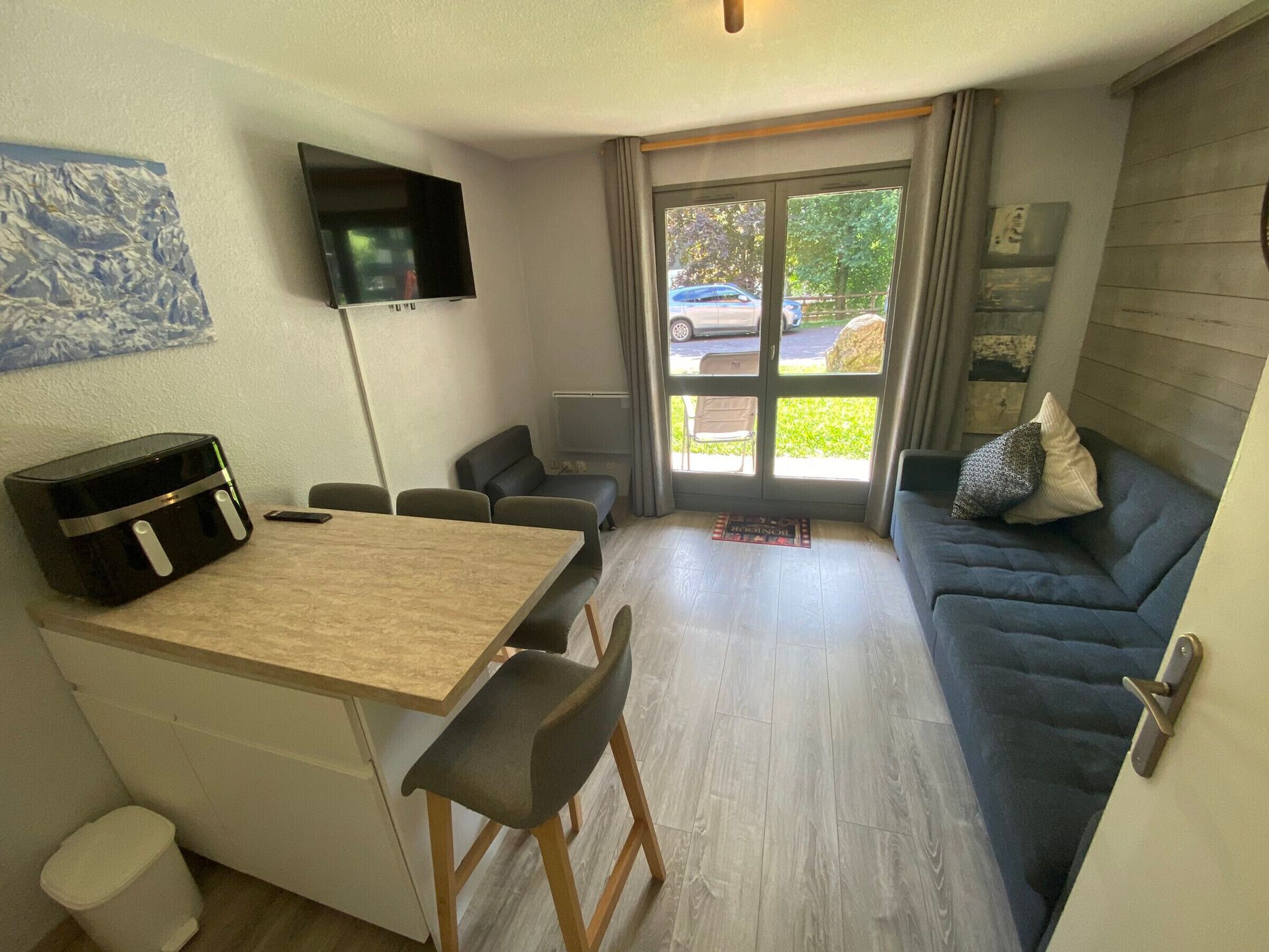 A compact living space with a kitchenette, a dining area, a seating area with a sofa, and a television mounted on the wall.
