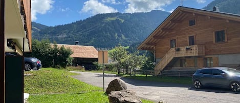 A wooden building with a balcony, a parked car, and a mountain backdrop.