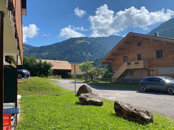 A wooden building with a balcony, a parked car, and a mountain backdrop.