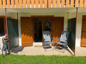 A covered outdoor area with two chairs and a bicycle, wooden doors, and a view into a building.