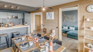 A modern kitchen with a dining area, wooden walls, and a blue sofa in the living room. - Premium 4* Apartment - 5 rooms for 8 people with Wifi (Tignes)