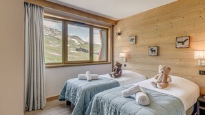 A room with two beds, a large window with a view of mountains, wooden walls, and a teddy bear on one bed. - Premium 4* Apartment - 5 rooms for 8 people with Wifi (Tignes)