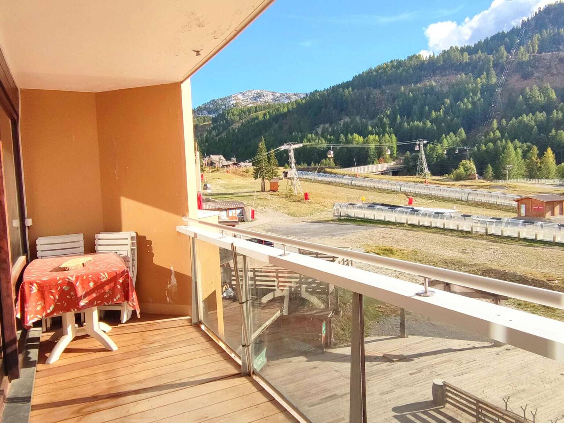 Ein Balkon mit Tisch und Stühlen, der auf Gleise und eine gebirgige Landschaft blickt.
