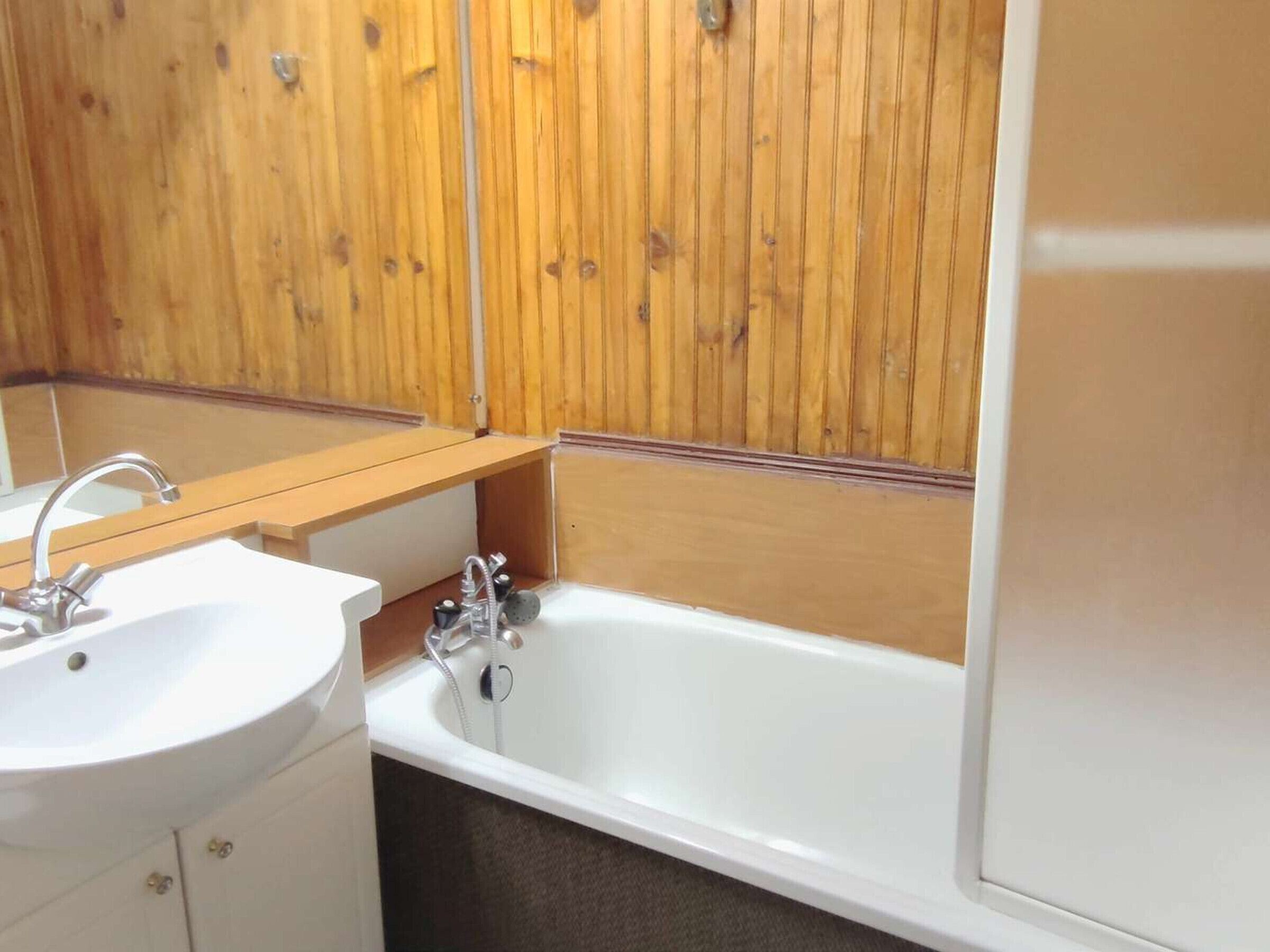 A bathroom with a wooden panel wall, a sink, and a bathtub.
