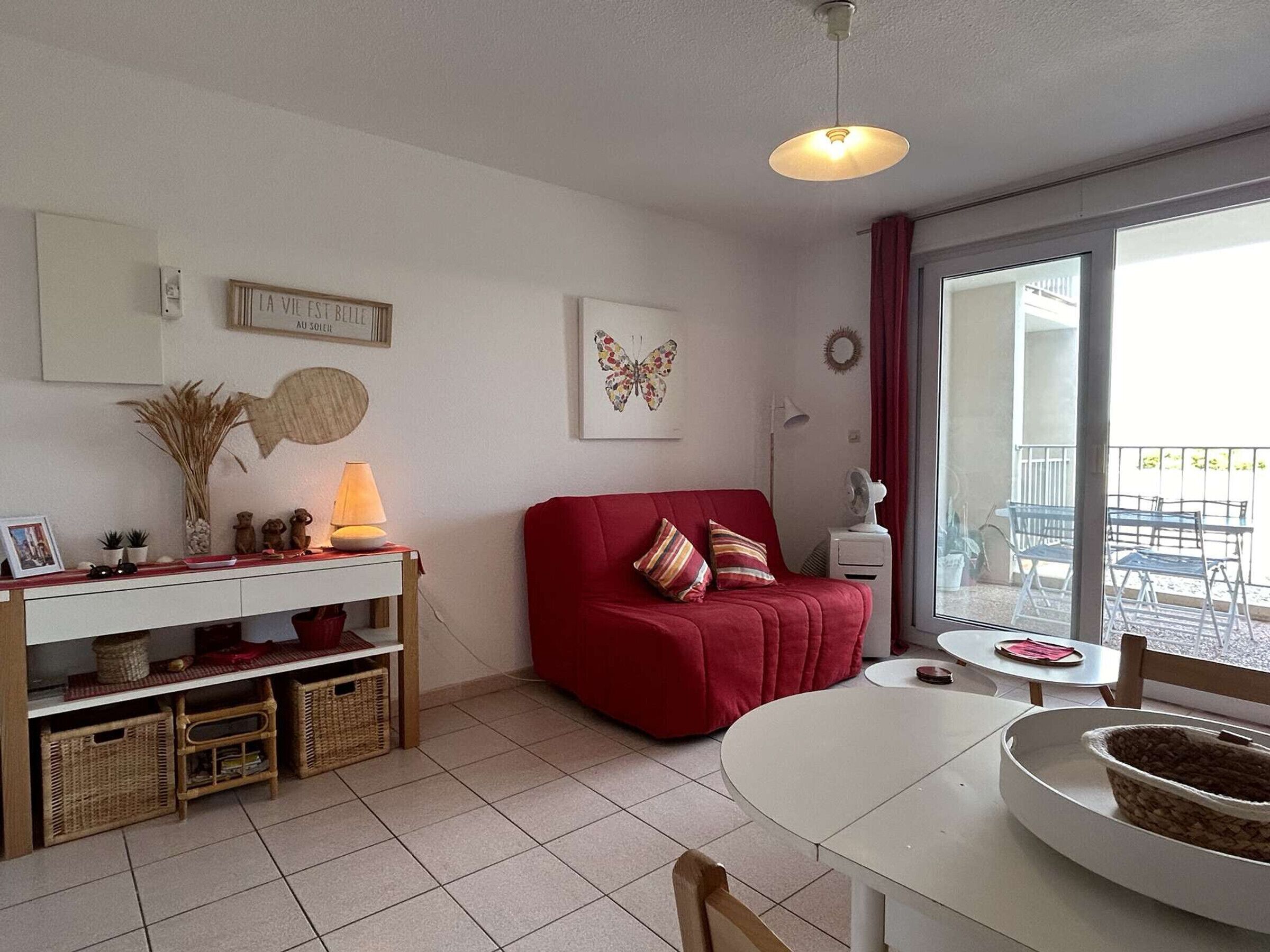 Una sala de estar acogedora con un sofá rojo, una mesa blanca y un balcón con mobiliario de exterior.
