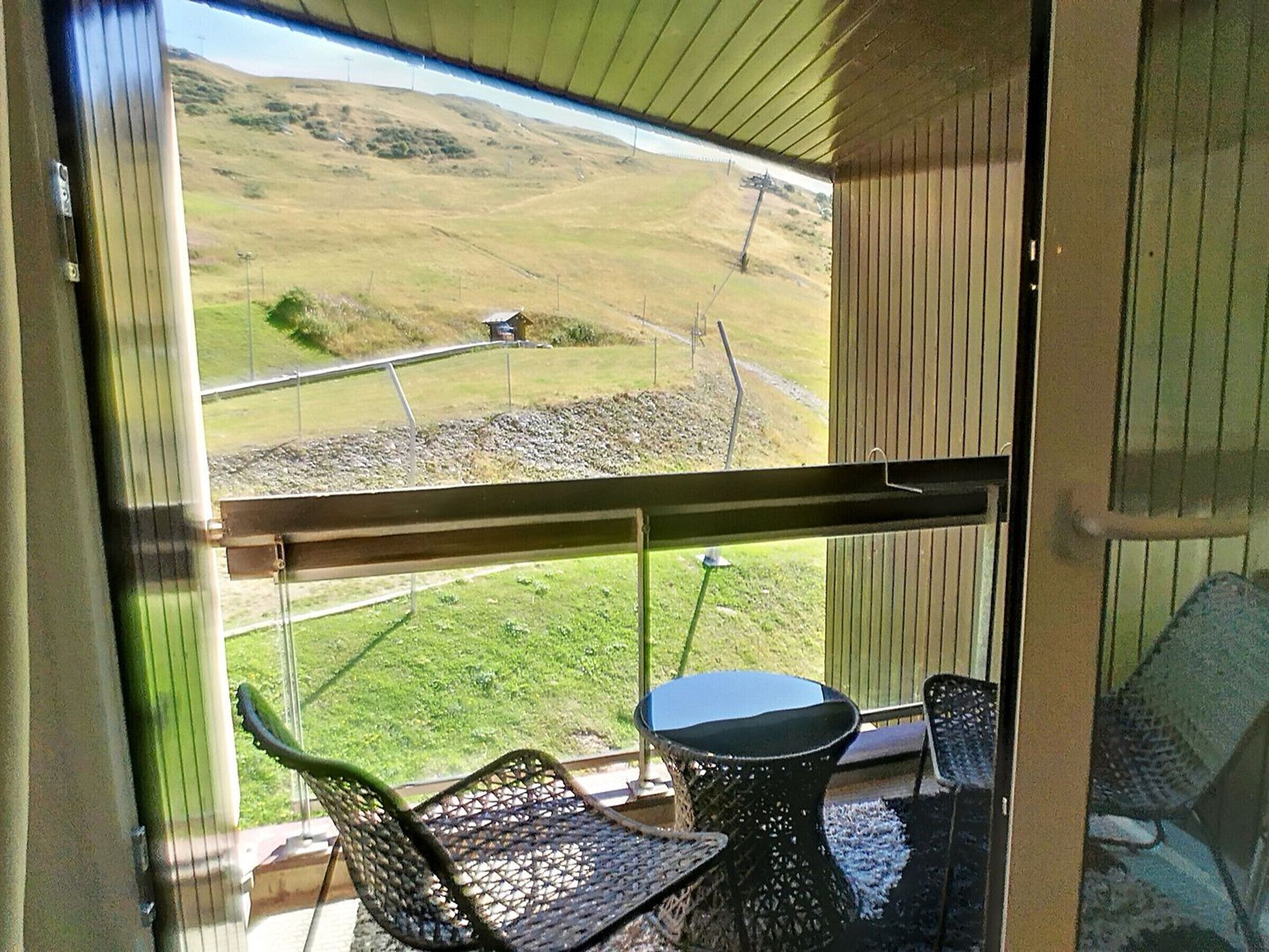 Ein Balkon mit Tisch und Stühlen, mit Blick auf eine grüne Landschaft, eine Straße und ein Gebäude in der Ferne.