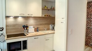 Moderni keittiö, jossa on valkoiset kaapit, puinen työtaso, sisäänrakennettu uuni ja keittiön vieressä oleva tiiliseinä.