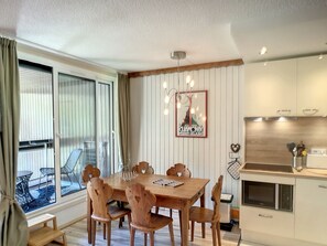 Une cuisine moderne avec des meubles blancs, une table à manger en bois avec six chaises et une grande fenêtre avec des rideaux.