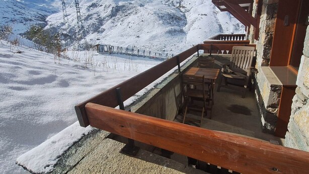 Un balcón de madera con vistas a montañas nevadas y un telesilla.