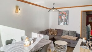 Un salon moderne avec un canapé gris, une table à manger recouverte d’une nappe à motifs et un luminaire suspendu.