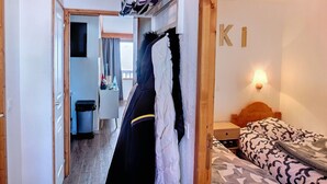 Un couloir étroit mène à une chambre à coucher qui contient un lit, une table de chevet et une lampe fixée au mur.