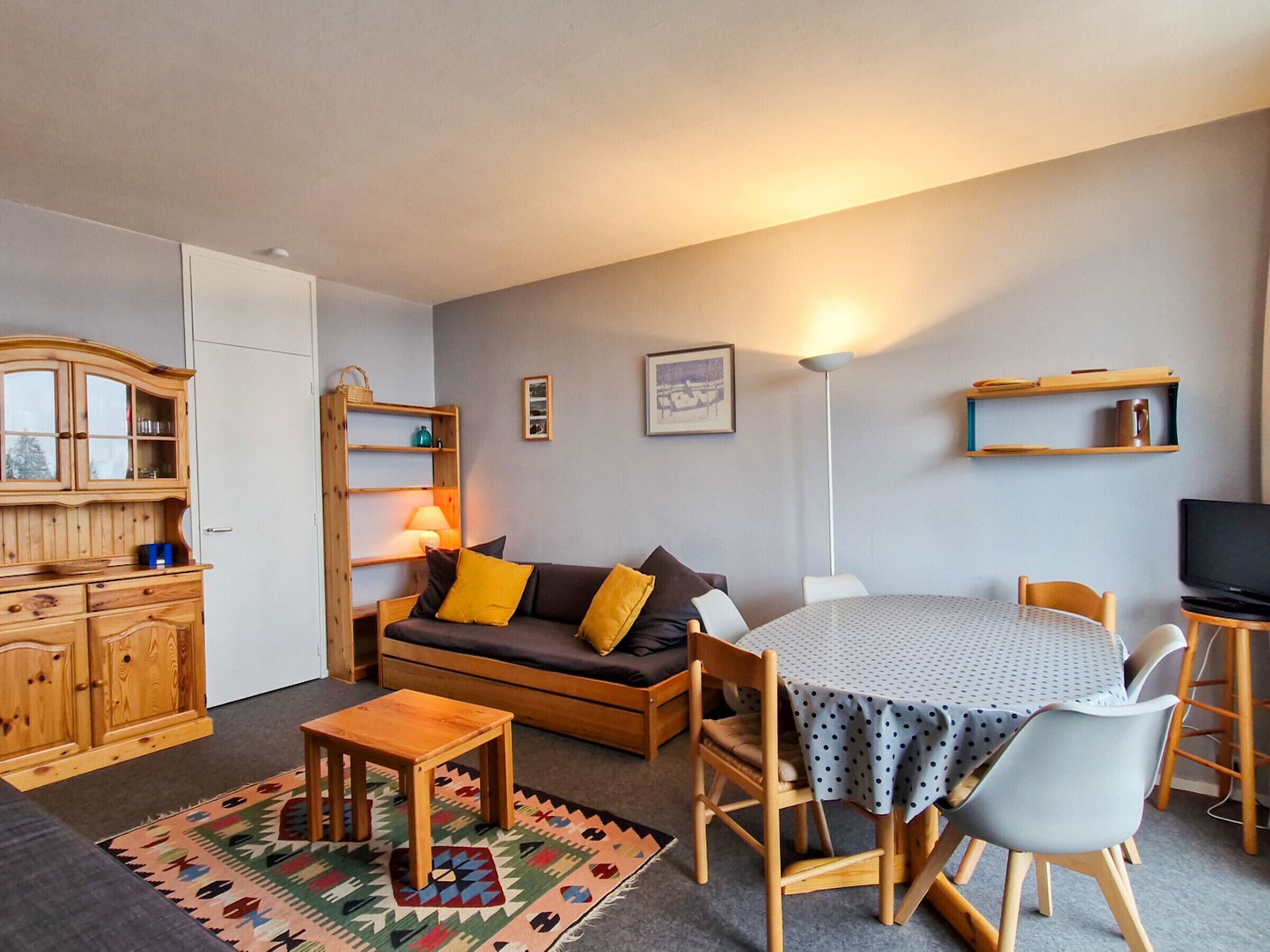 Een gezellige woonkamer met een bank, een eettafel en een keukenhoek met houten kastjes en een lamp.