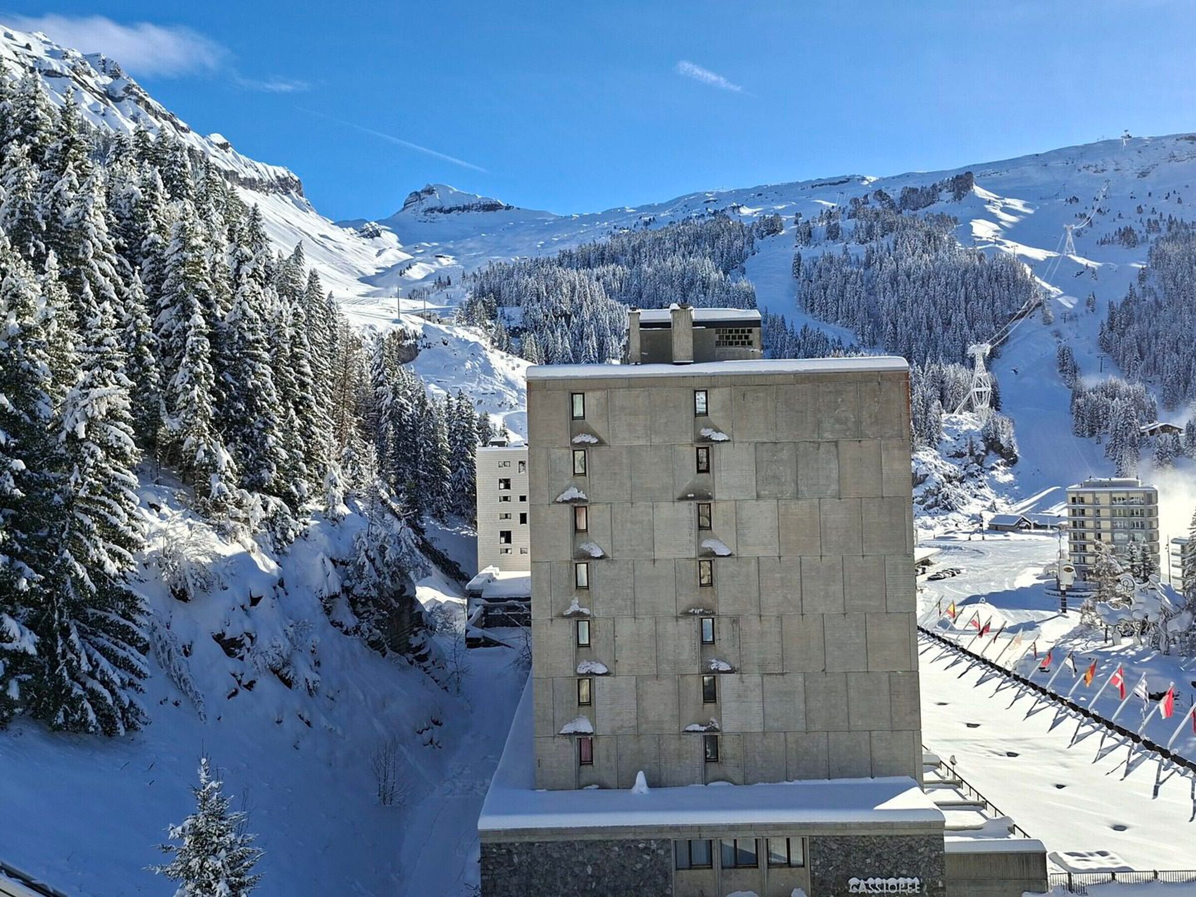 A snow-covered mountain with a ski resort, a concrete building with multiple windows, and a ski lift in the background.