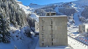 Une montagne enneigée avec une station de ski, un bâtiment en béton doté de nombreuses fenêtres et un télésiège en arrière-plan.