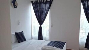 A hotel room with a large bed, two bedside tables, a window with curtains, an air conditioning unit, and a view of the outdoors. - 3 Chambres Salon (Saint Louis)