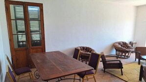 A dining area with a wooden table and four chairs, a pet bed, and a wicker chair. - 3 Chambres Salon (Saint Louis)