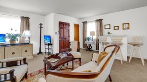 Ein Wohnzimmer mit einer Couch, Sesseln, einem Couchtisch, einem Fernseher, einem Essbereich mit Tisch und Stühlen sowie einer Tür, die in einen anderen Raum führt.